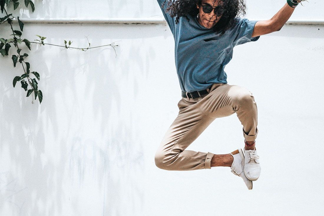 A man dressed in a blue t-shirt and beige pants is jumping excitedly into the air with his hands up